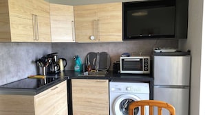 A compact kitchen with wooden cabinets, a microwave, a toaster, a washing machine, and a sink.