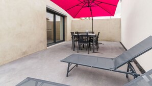 A patio with a table and chairs, a red umbrella, and two lounge chairs.