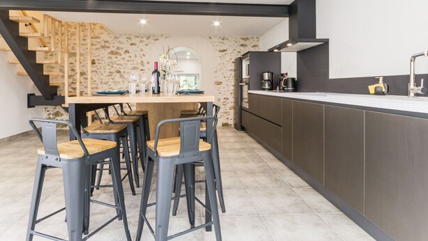 A modern kitchen with dark cabinetry, a central island with bar stools, and a stone accent wall.