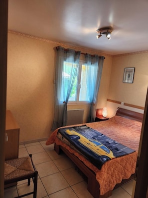 Quarto com cama, cadeira, janela com cortinas, luminária de cabeceira e luminária no teto.