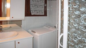 A bathroom with a sink, a washing machine, and a shower with a patterned curtain.