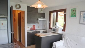 A compact kitchen with a microwave, sink, and stove. There is a small dining area with a table and a bed with a white cover.