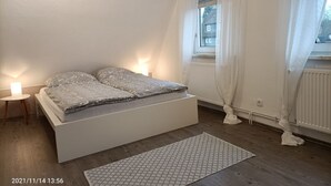 A bedroom with a bed, bedside lamps, a window with curtains, and a radiator. - Vacation apartment/holiday home for up to 5 people (children under 6 free of charge) (Clausthal-Zellerfeld)