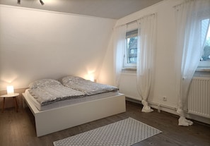 Une chambre à coucher avec un lit, des lampes de chevet, une fenêtre avec des rideaux et un radiateur.