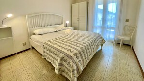 A neatly arranged bedroom with a bed, bedside lamps, a chair, and a window with curtains. - Amazing villa with private garden (Porto Santa Margherita)