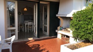 A patio with a white chair, a small table, and a potted plant. - Amazing villa with private garden (Porto Santa Margherita)