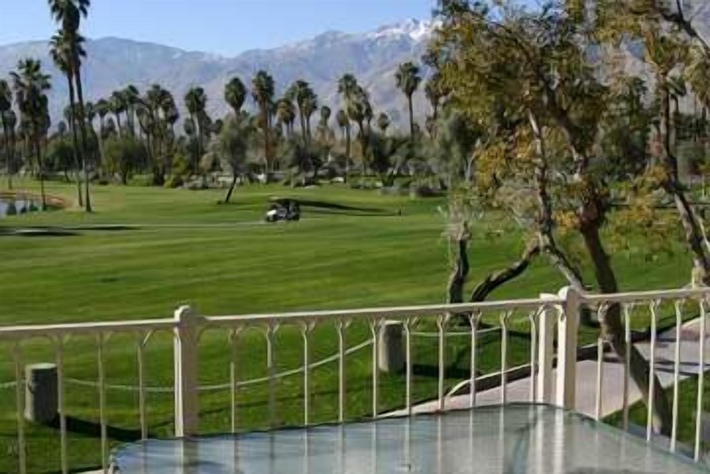 A golf course with a clear view of the green, a distant mountain range, and a few palm trees.