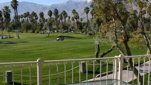 Un campo de golf con vista despejada al green, una cadena montañosa distante y algunas palmeras.