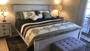 Un dormitorio con una cama grande, dos mesitas de noche, un banco y un cuadro en la pared.