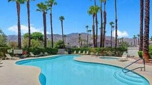 Una piscina con palmeras y sillas de descanso, rodeada de montañas.