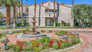 Un edificio con una fuente en el centro, rodeado por un jardín con diversas plantas y flores.