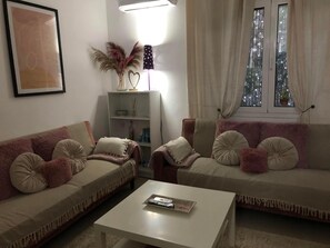 A living room with two sofas, a coffee table, a bookshelf, and a window with curtains.