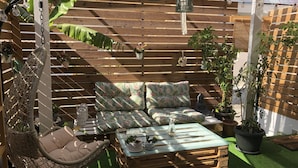Een gezellig buitenverblijf met een hangstoel, een comfortabele bank en een bijzettafeltje, omgeven door houten lamellen en plantenpotten.