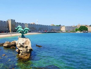 A coastal area with a clear view of a historic stone wall, a rocky outcrop with a sculpture, and a calm sea. - Casa Fiore - 2 Bed House 10 Mins Walk to Centre (Rhodes)
