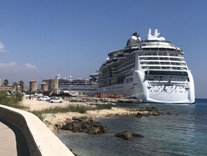 A large cruise ship docked at a port with multiple decks and balconies, surrounded by a sandy beach and rocky shoreline. - Casa Fiore - 2 Bed House 10 Mins Walk to Centre (Rhodes)