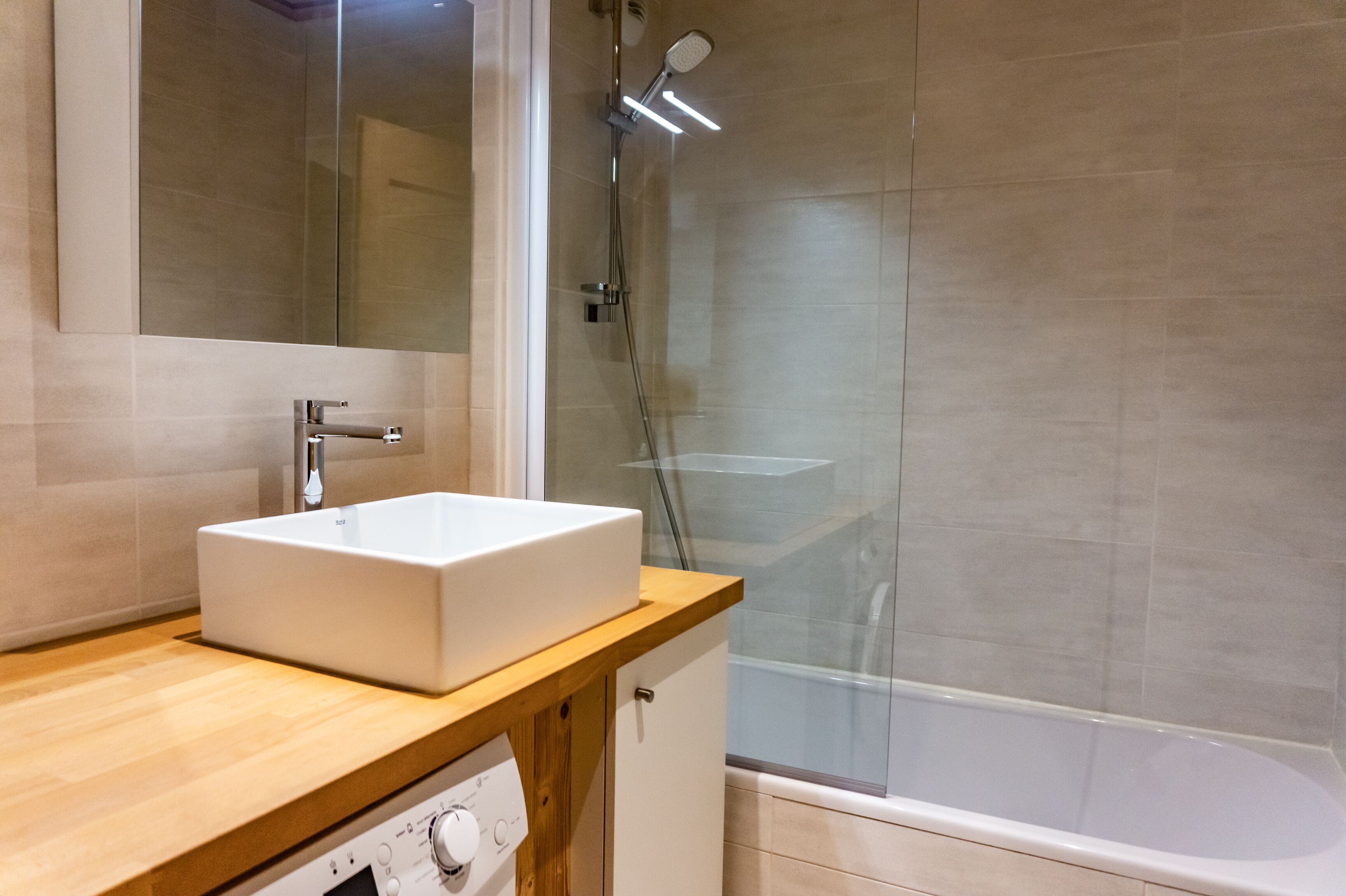Ein modernes Badezimmer mit einem weißen Waschbecken, einer Holzarbeitsplatte und einer Duschkabine aus Glas.