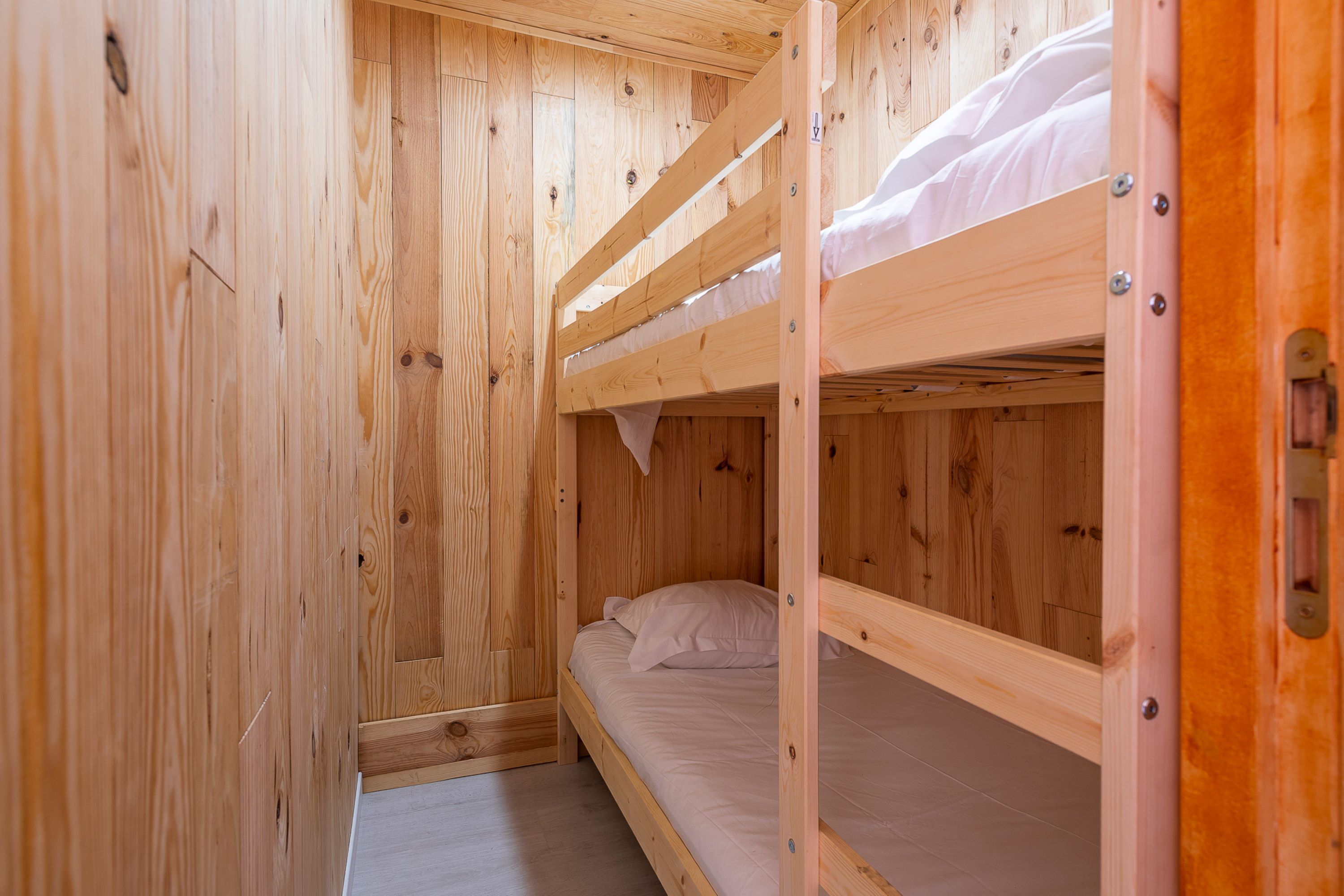 A wooden bunk bed room with a single bed and a lower bunk.