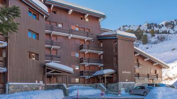 A multi-story wooden building with balconies, a ski slope in the background, and a sign reading "Les Proveres."