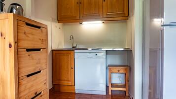 A compact kitchen with wooden cabinets, a dishwasher, and a small wooden table.