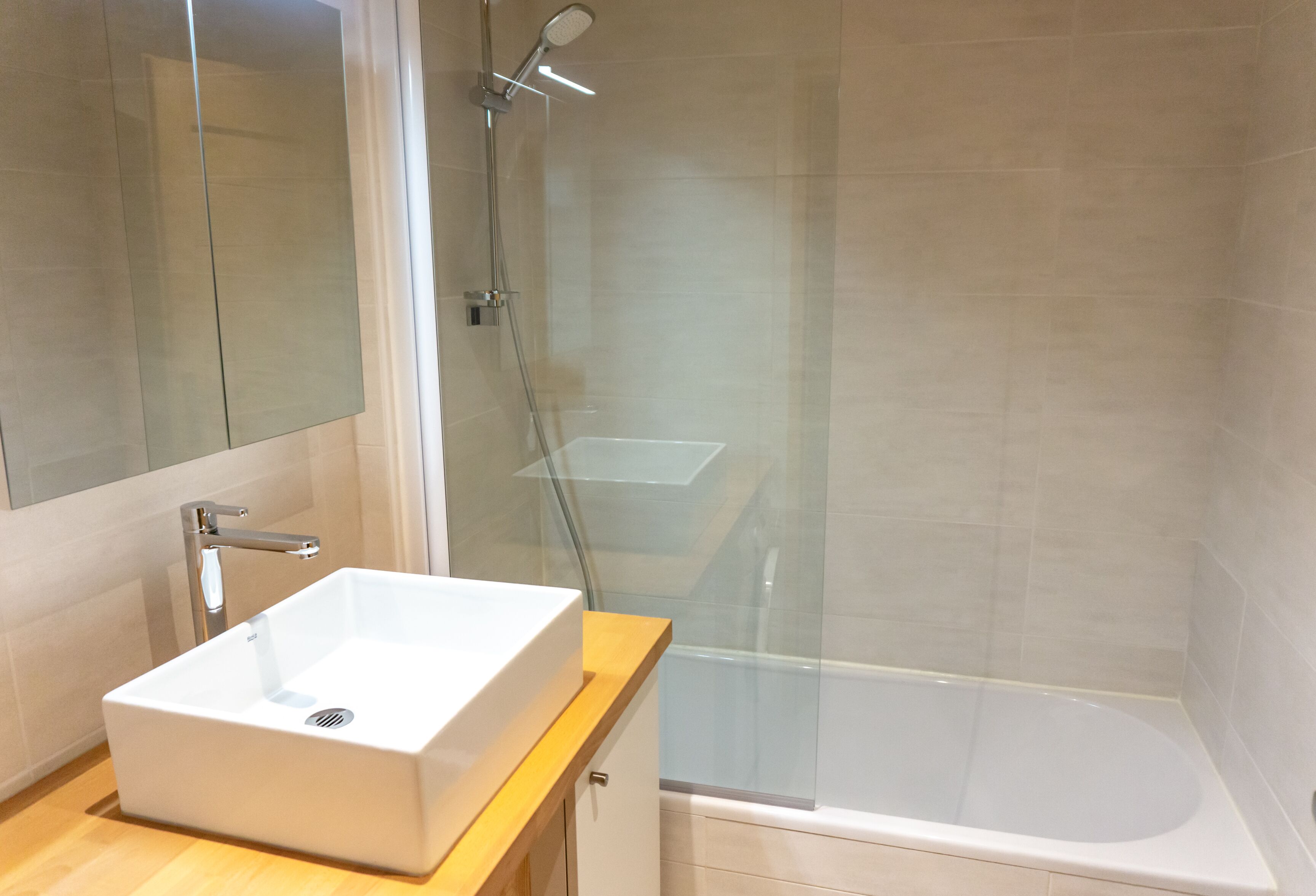A modern bathroom with a white sink, a glass shower enclosure, and a bathtub.