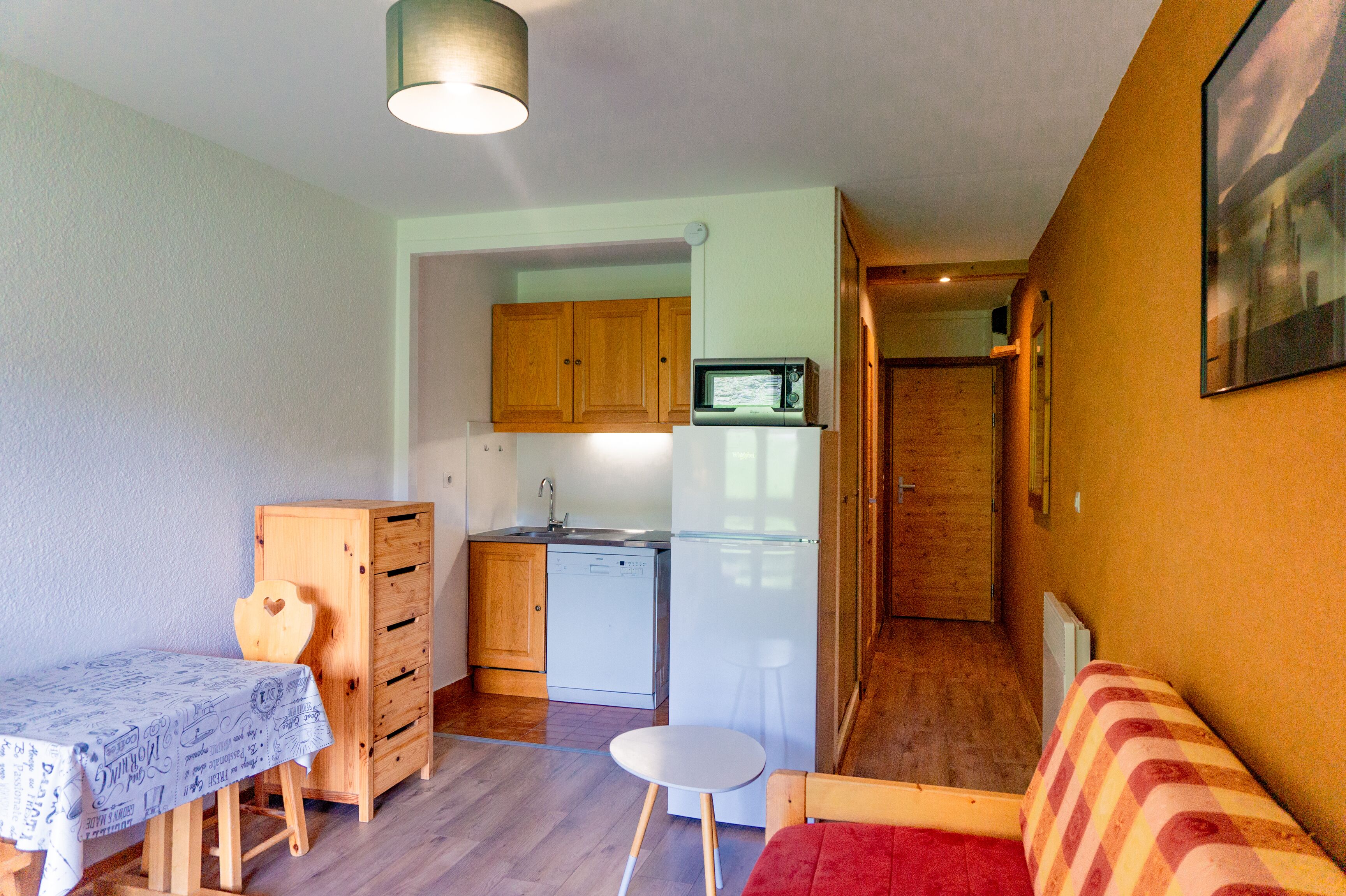 A compact living space with a kitchenette, a dining table, a sofa, and a small stool.