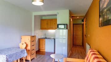 A compact living space with a kitchenette, a dining table, a sofa, and a small stool.