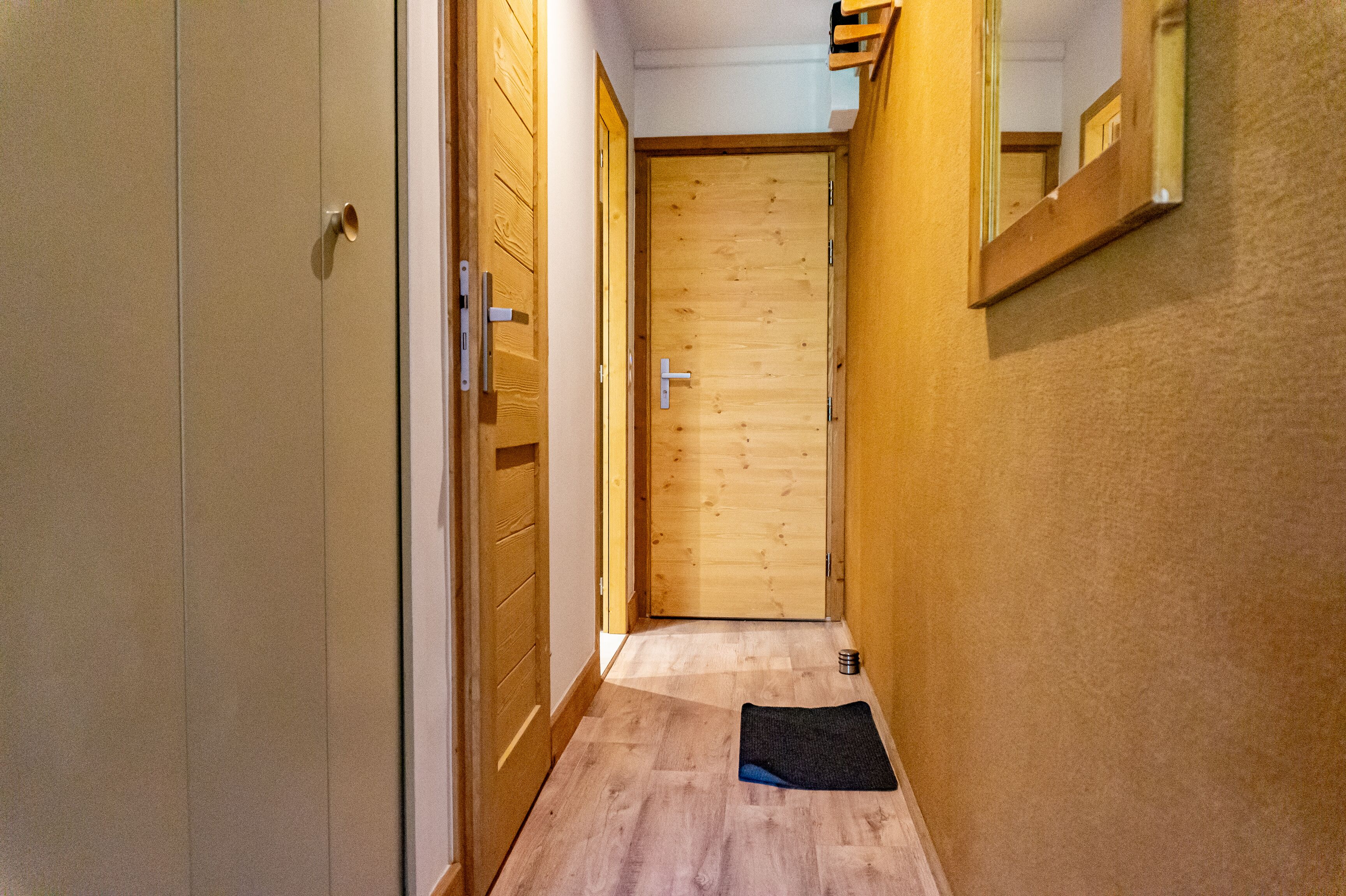 A narrow hallway with wooden flooring, a door at the end, and a small rug on the floor.
