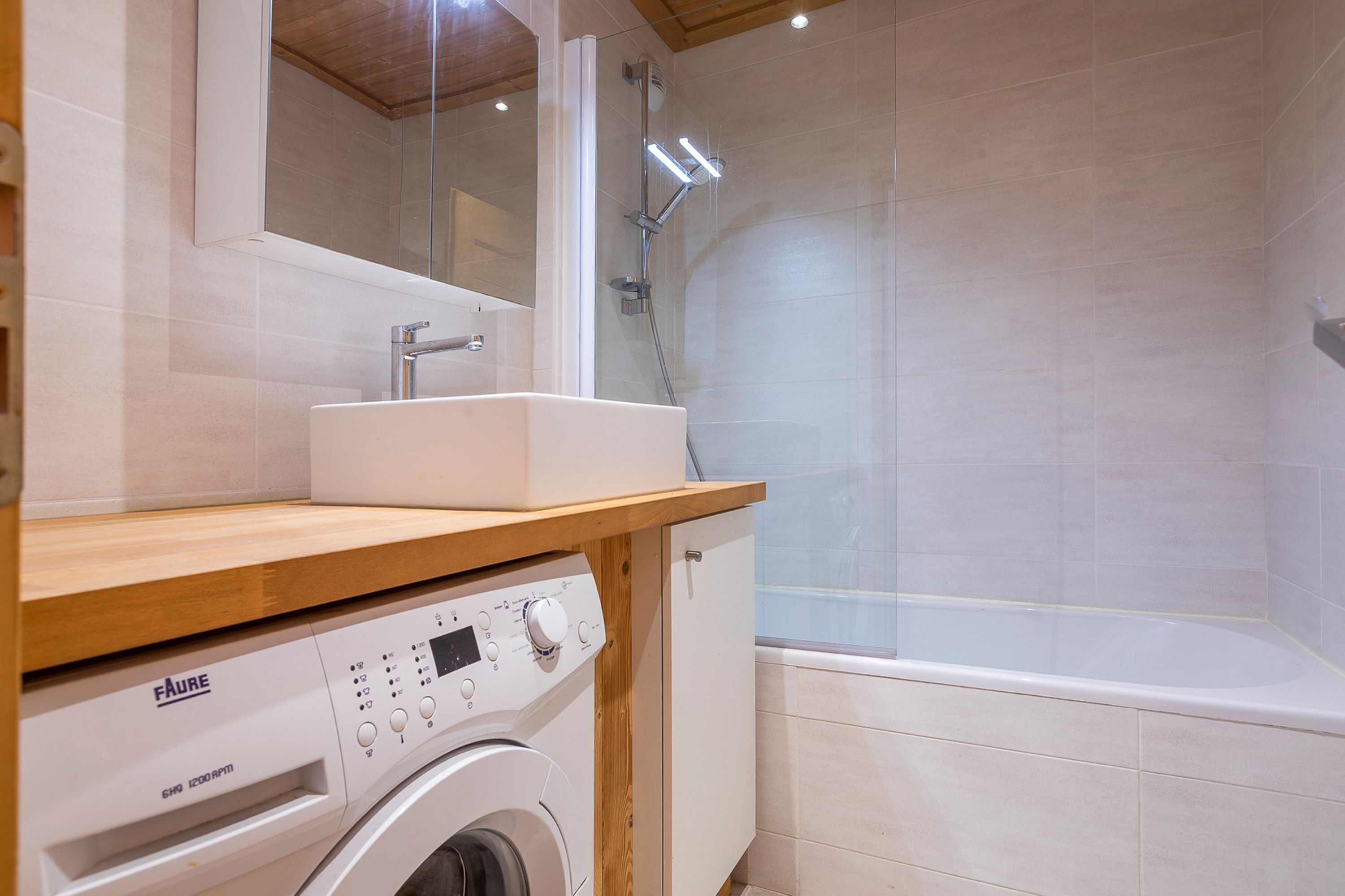 Une salle de bain moderne équipée d’un lave-linge intégré, d’un évier et d’un espace douche.