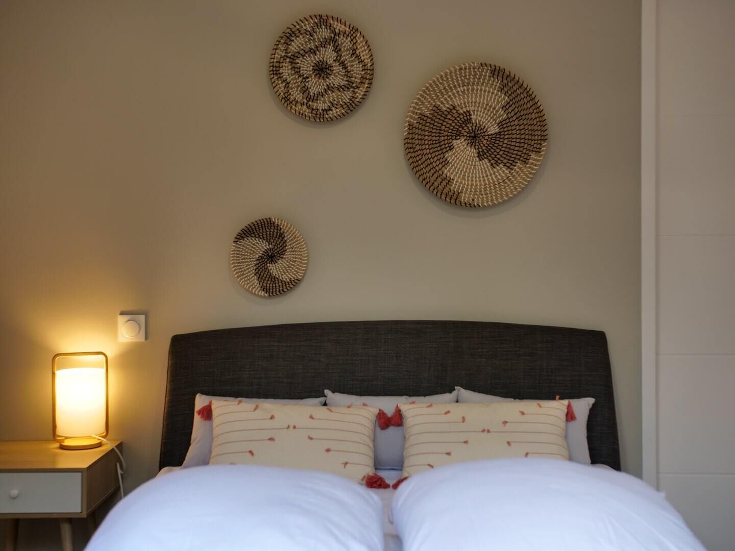 A neatly made bed with white linens and patterned pillows, a dark headboard, and three circular wall decorations.