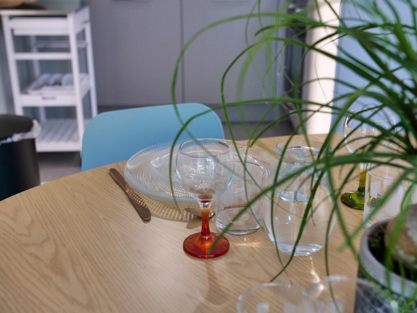 Une table ronde en bois, sur laquelle on trouve de la vaisselle en verre transparent, une bougie rouge et une plante en pot.