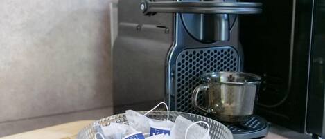 En kaffebryggare, en glasmugg och en korg med tepåsar står på en bänkskiva.