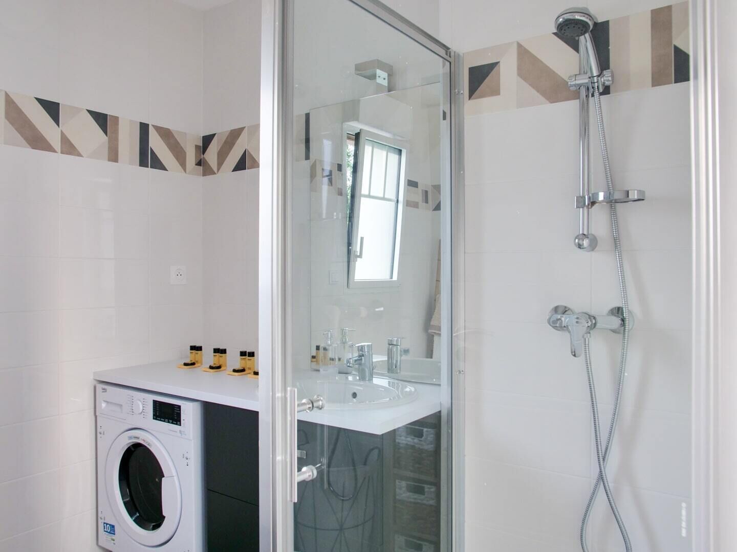 Un baño moderno con ducha acristalada, lavadora integrada y tocador con espejo.