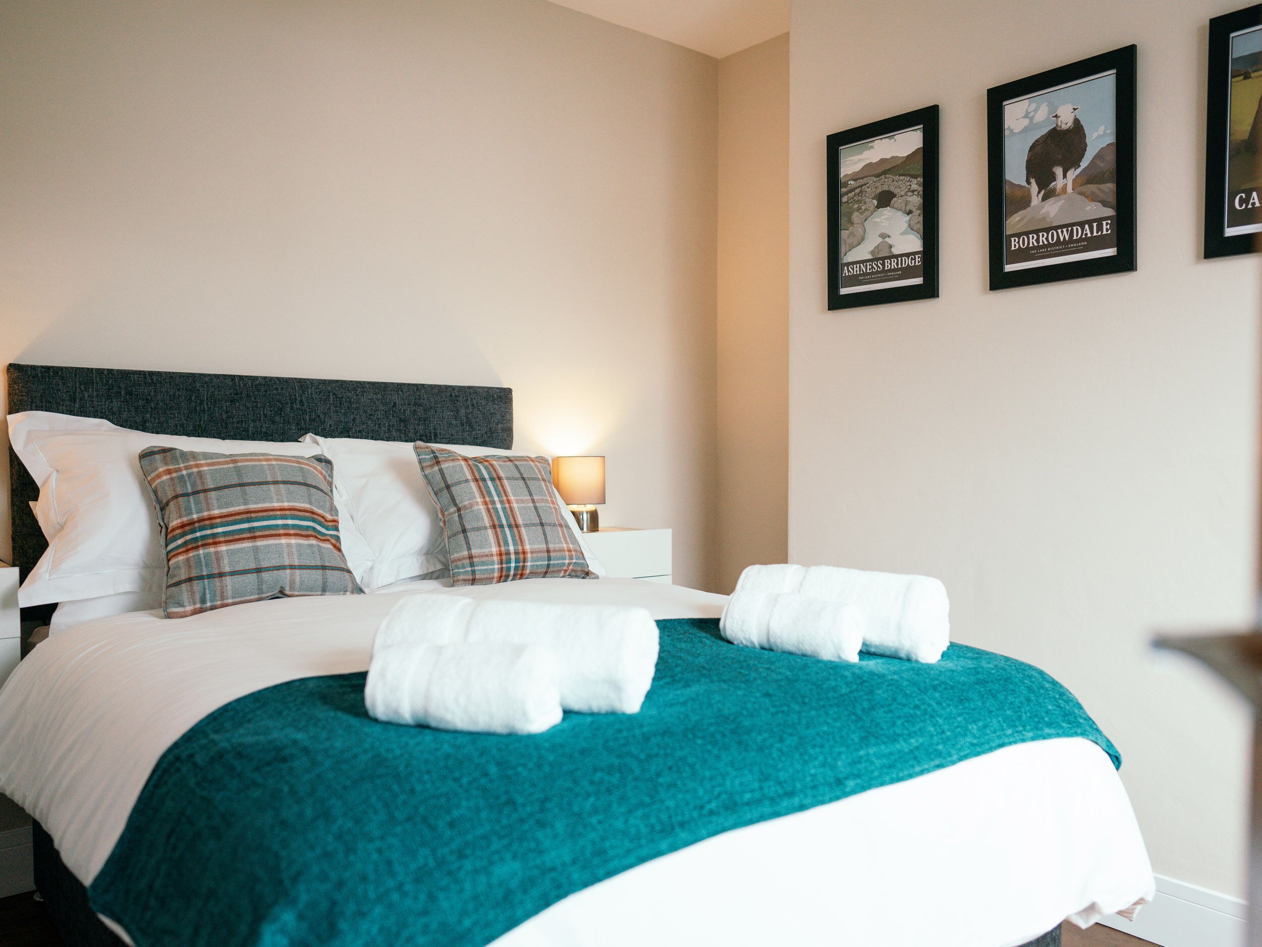 Un lit bien fait, recouvert d’une couverture turquoise, avec deux oreillers et deux serviettes blanches.