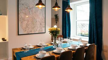 A dining area with a wooden table set for four, a map on the wall, and a window with curtains.
