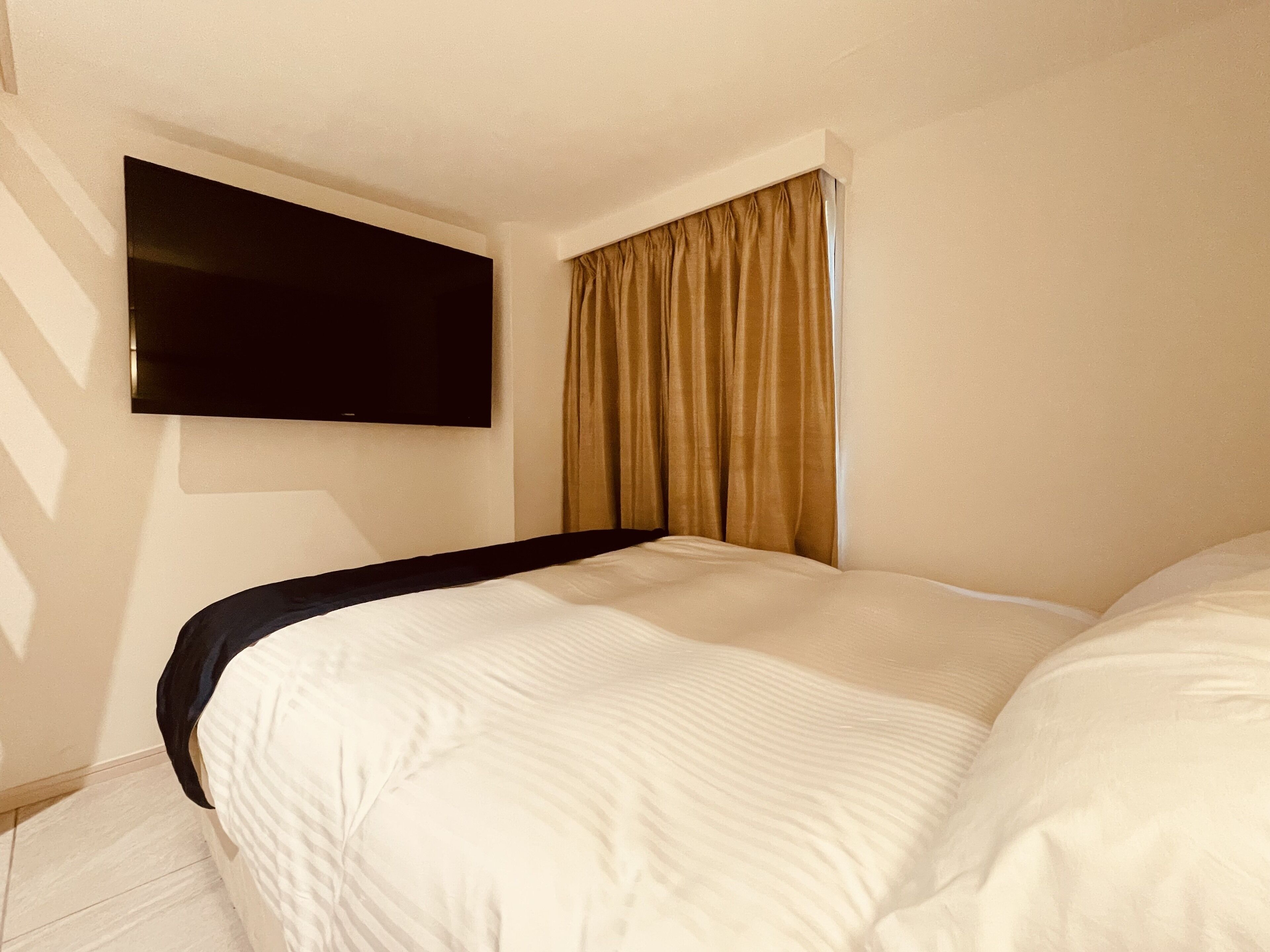 Une chambre d’hôtel avec un lit, un téléviseur à écran plat fixé au mur et une fenêtre avec des rideaux.