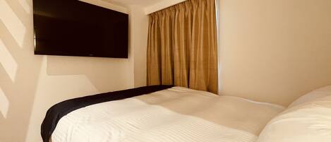 Une chambre d’hôtel avec un lit, un téléviseur à écran plat fixé au mur et une fenêtre avec des rideaux.
