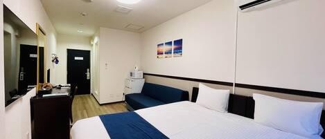 Une chambre d’hôtel équipée d’un lit, d’un bureau, d’une chaise, d’un four à micro-ondes et d’un climatiseur fixé au mur.
