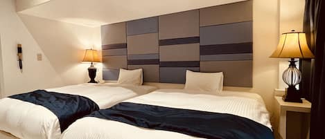 A hotel room with two beds, a large padded headboard, bedside lamps, and a telephone on the wall.