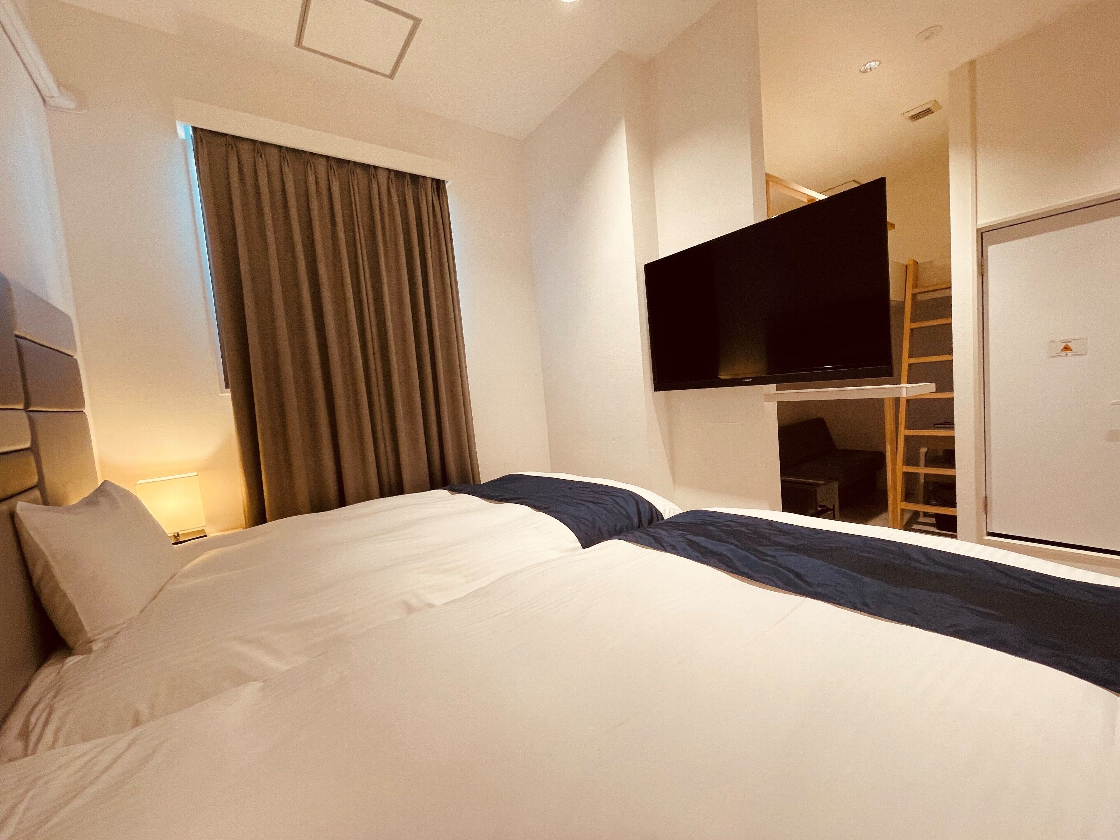 A hotel room with a bed, a TV mounted on the wall, a wardrobe, and a window with curtains.