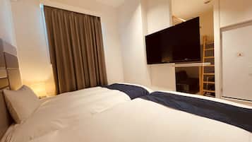A hotel room with a bed, a TV mounted on the wall, a wardrobe, and a window with curtains.
