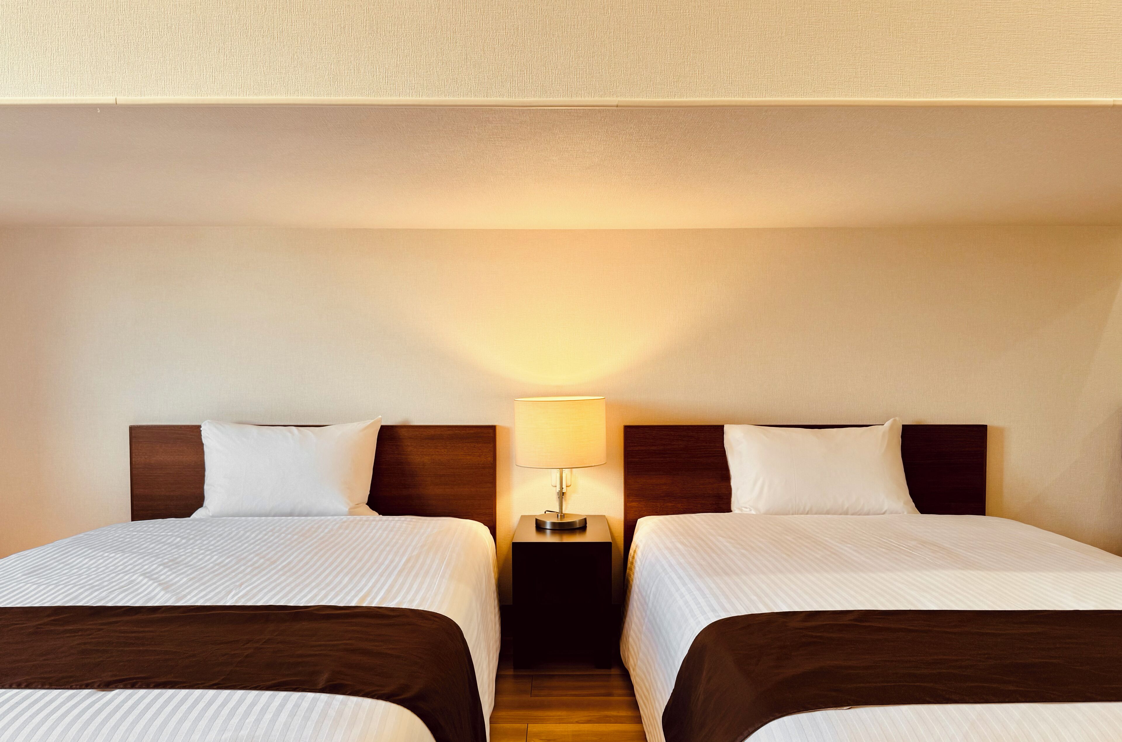 A hotel room with two beds, a nightstand with a lamp, and a wooden headboard.