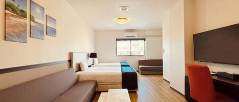 A hotel room with two beds, a sofa, a TV, and a desk.