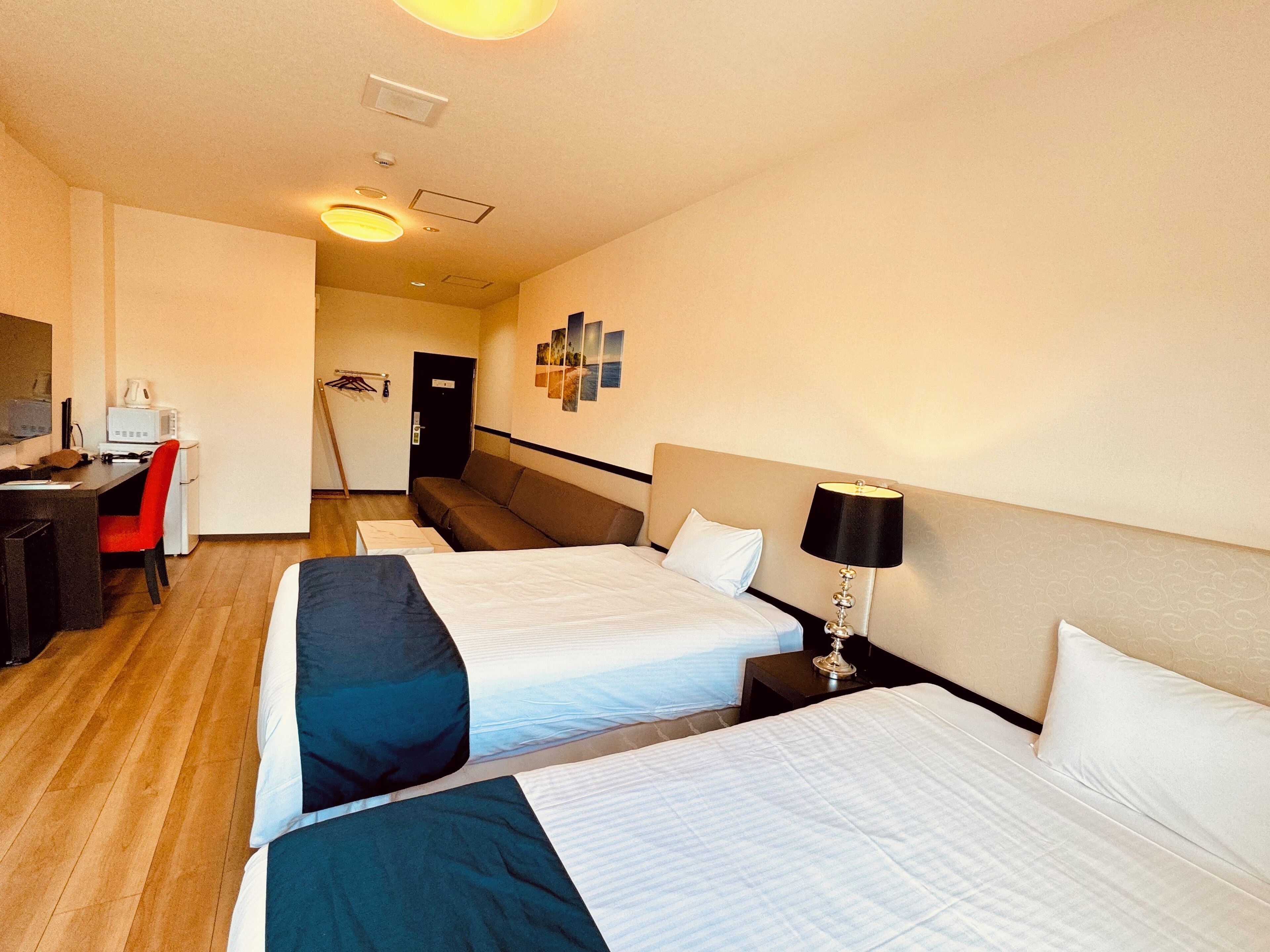 Ein Hotelzimmer mit zwei Betten, einem Schreibtisch, einem Stuhl, einer Mikrowelle und einem an der Wand montierten Fernseher.