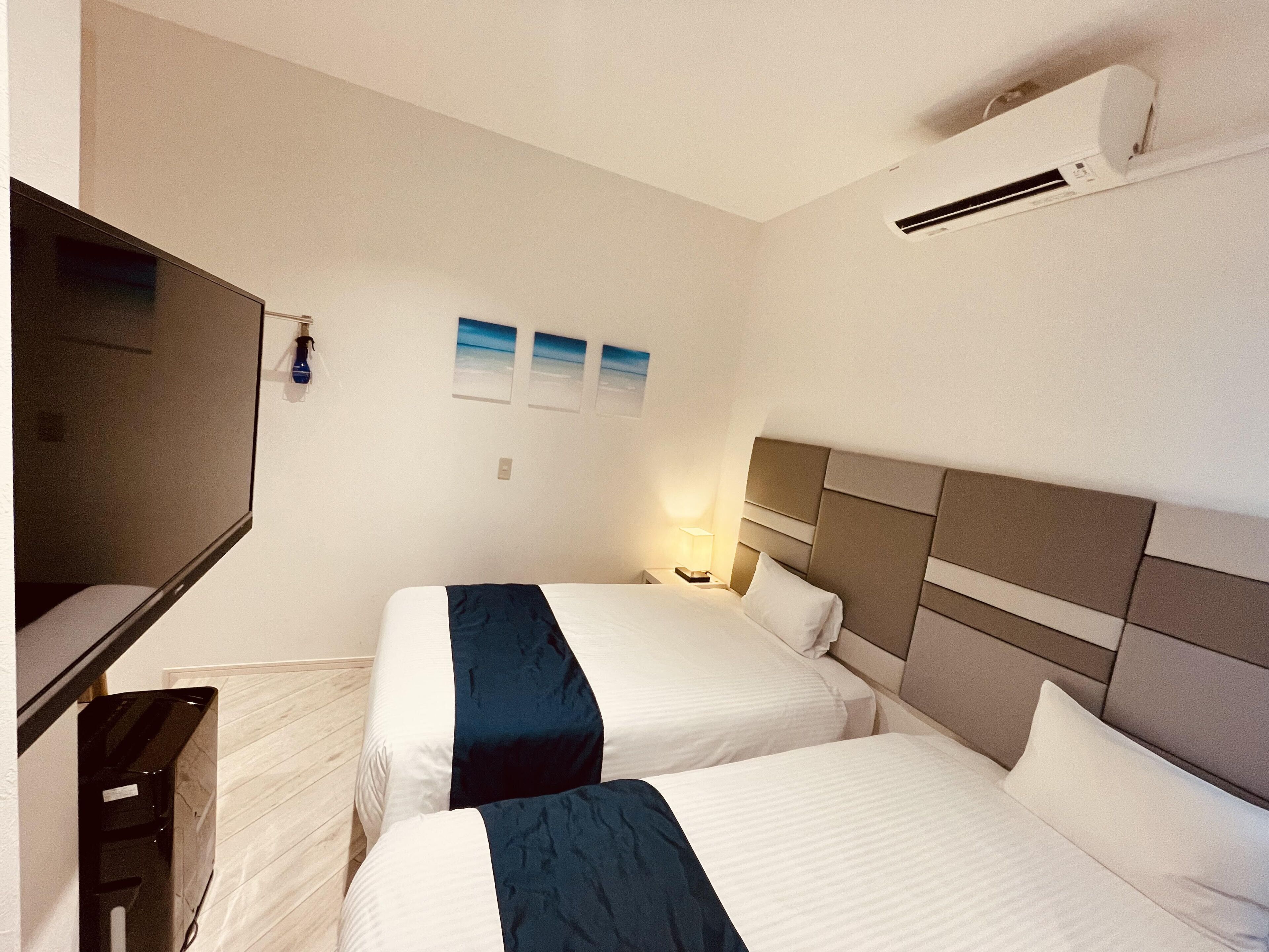 A hotel room with two beds, a TV, and an air conditioning unit.
