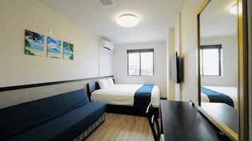 Quarto de hotel com uma cama, um sofá, uma mesa e um espelho grande. Há três quadros na parede e uma janela com vista para edifícios.