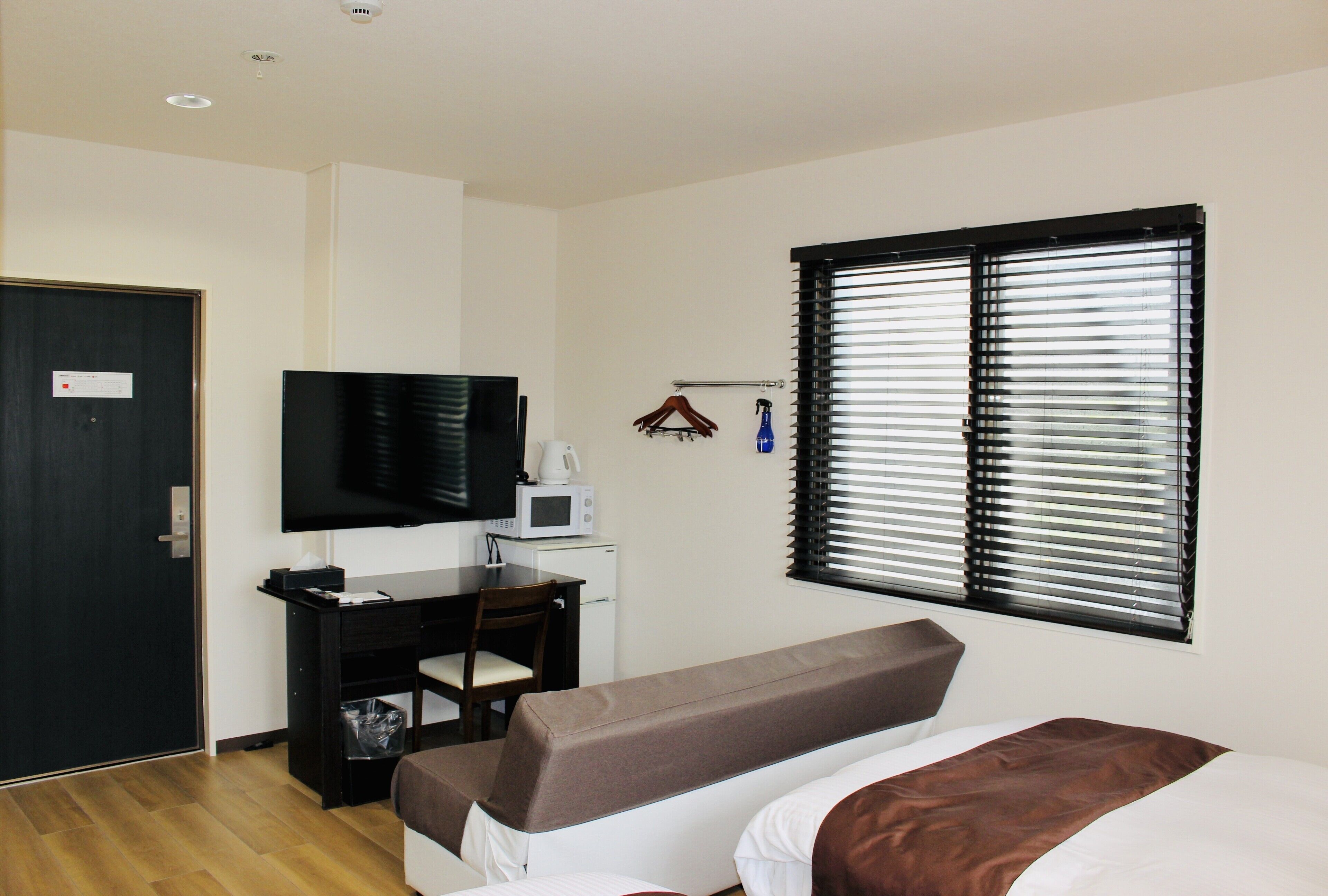 Ein Hotelzimmer mit einem Bett, einem Schreibtisch mit Computer, einem Fernseher und einem Fenster mit Jalousien.