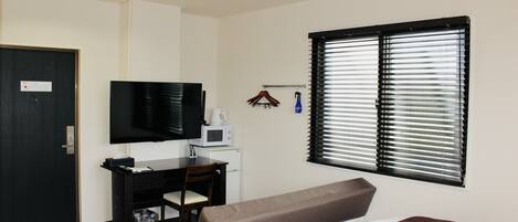 A hotel room with a bed, a desk with a computer, a television, and a window with blinds.