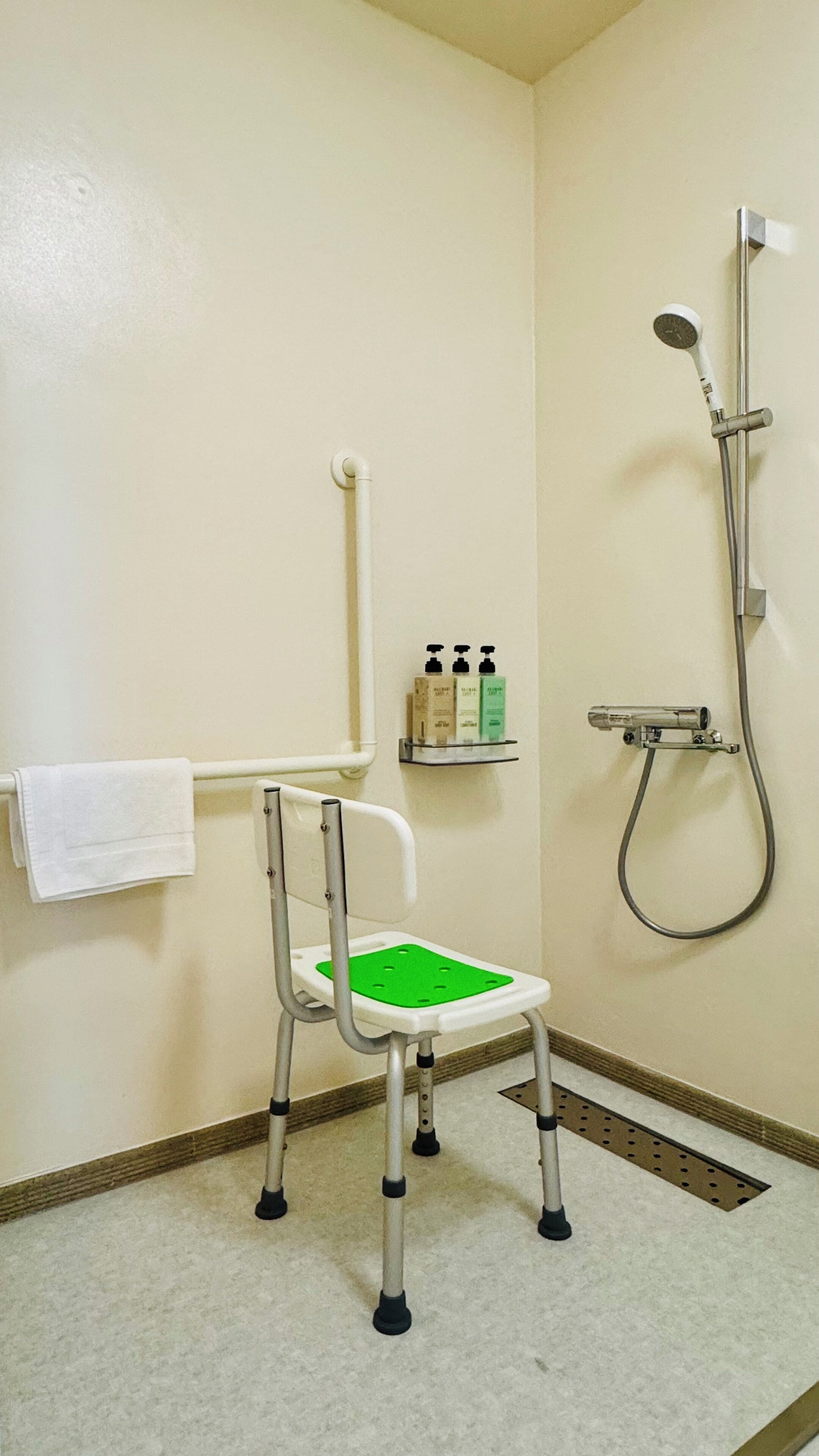 A bathroom with a wheelchair-accessible shower chair, a towel rack, and a shelf with toiletries.