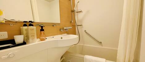 A bathroom with a white sink, mirror, and shower. There are toiletries on the counter and a towel hanging on the wall.
