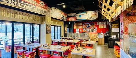Interior de un restaurante con varias mesas y taburetes, vigas de madera en el techo y diferentes letreros y carteles en las paredes.